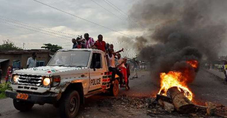 Protestors opposed to the Burundian president Pierre Nkurunziza's third term in office hitch a ride on a police vehicle past a burning barricade during a demonstration in the Cibitoke neighborhood of Bujumbura on May 19, 2015. By Carl De Souza (AFP)