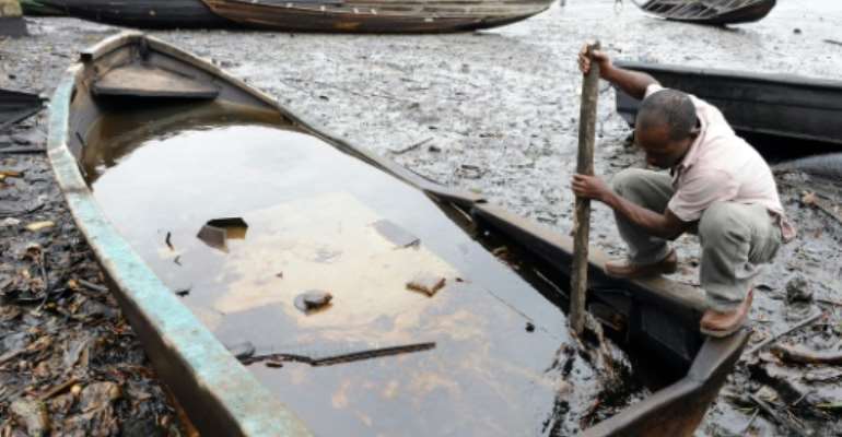 An indigene of Bodo, in Nigeria's Ogoniland region, tries to separate with a stick the crude oil from water in a boat at the Bodo waterways, polluted by oil spills attributed to Shell equipment failure, August 11, 2011. By Pius Utomi Ekpei (AFP/File)