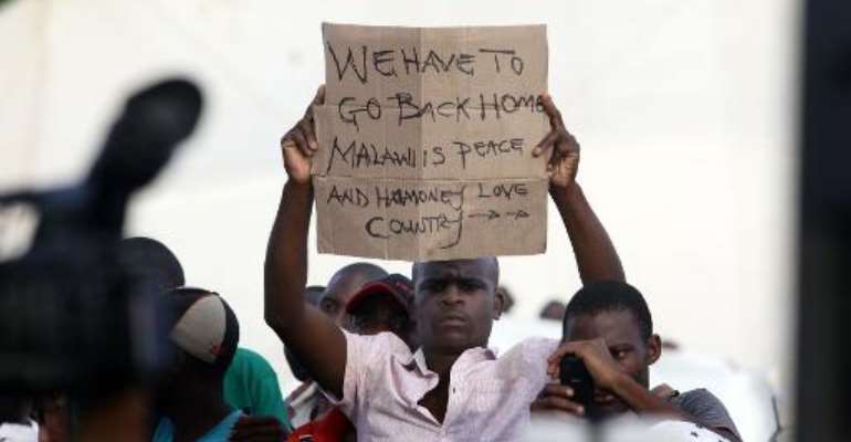 A foreign national shows a sign as South African President Jacob Zuma addresses a temporary refugee camp in Chatsworth, south of Durban on April 18, 2015 during a visit marked by hostile reaction. By Rajesh Jantilal (AFP)