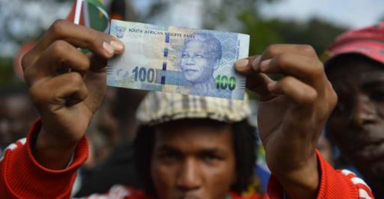 A man holds a 100 rand bill bearing the portrait of South African former president Nelson MandelaMandela as Mandela's funeral cortege drives through the streets in Pretoria on December 11, 2013. By Odd Andersen (AFP/File)