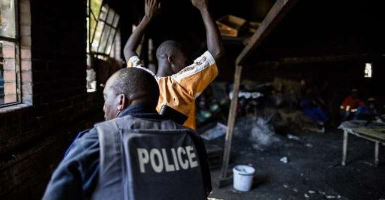 A resident raises his hands as a South African anti-riot police officer raids a hostel in Benoni on April 16, 2015. By Marco Longari (AFP)