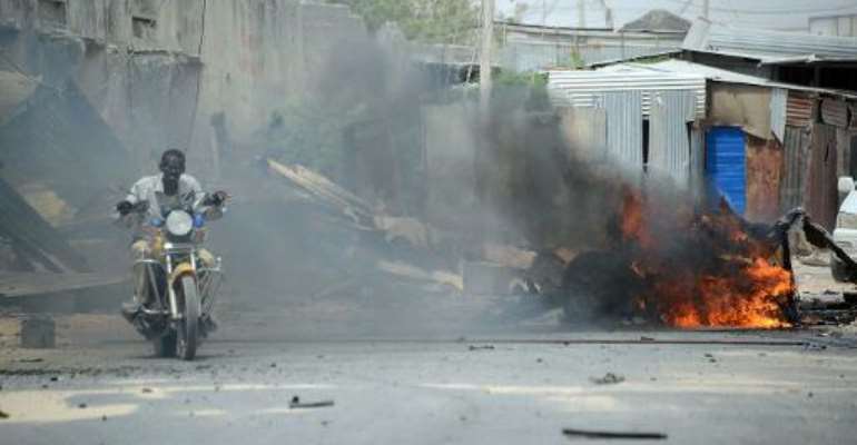 A man rides a motorbike past a burning car shortly after it exploded on February 13, 2014 near the entrance of Mogadishu's international airport. By Mohamed Abdiwahab (AFP)