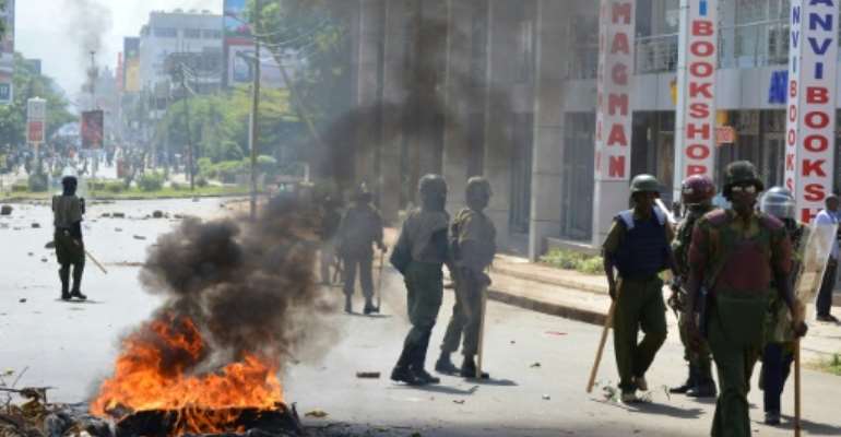 Police officers walk past burning tyres in Kisumu, Kenya, on June 6, 2016. By (AFP)