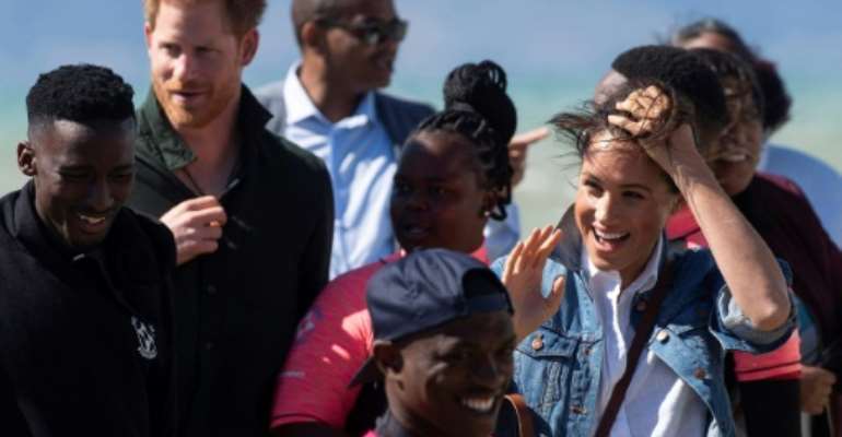 Wind and smiles: Prince Harry and his wife Meghan meet members of Waves for Change. The group uses surfing to help young people trapped in Cape Town's slums get a different perspective on life. By DAVID HARRISON (AFP)