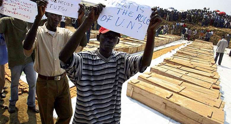 Men hold up protest signs in front of the coffins of DRC refugees killed in August 2004 in Gatumba, Burundi.  - Source: Simon MainaAFP via Getty Images