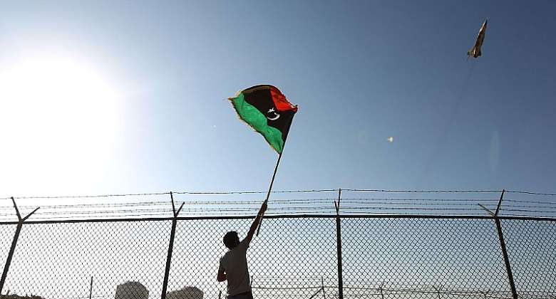 A man waves a Libyan flag as a fighter jet flies by Zueitina oil terminal in 2016.  - Source: Abdullah DomaAFP via Getty Images
