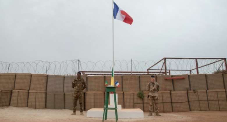 A Malian and a French soldier stand either side of a flagpole at a French base in Timbuktu before a ceremony last December to hand the facility over to the Malian military. Since then, France has announced a full pullout from Mali.  By FLORENT VERGNES AFP