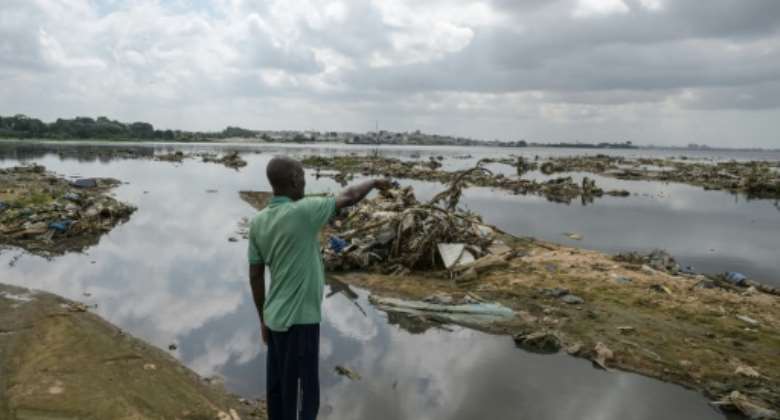 A resident points to plastic and other waste at a lagoon in Abidjan.  By Sia KAMBOU AFPFile