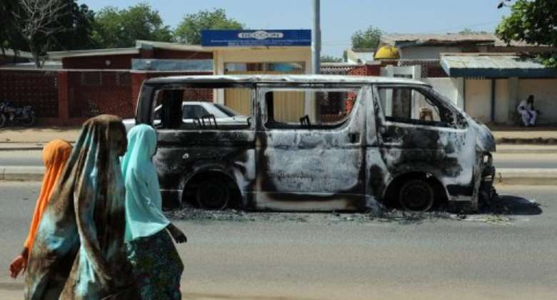Young girls walk past a vehicle burnt in 2011 on a street in Damaturu in northeastern Nigeria.  By Pius Utomi Ekpei (AFP/File)