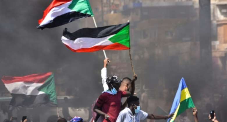 In this file picture taken on October 21, 2021, Sudanese demonstrators raise national flags as they take part in a protest in the city of Khartoum Bahri to demand the government's transition to civilian rule.  By - AFPFile