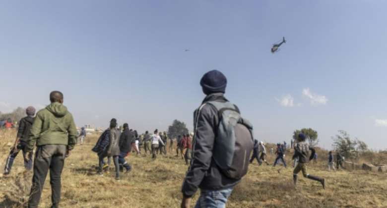 Residents run away from a police helicopter during a protest against illegal mining and rising crime in Kagiso.  By GUILLEM SARTORIO AFP