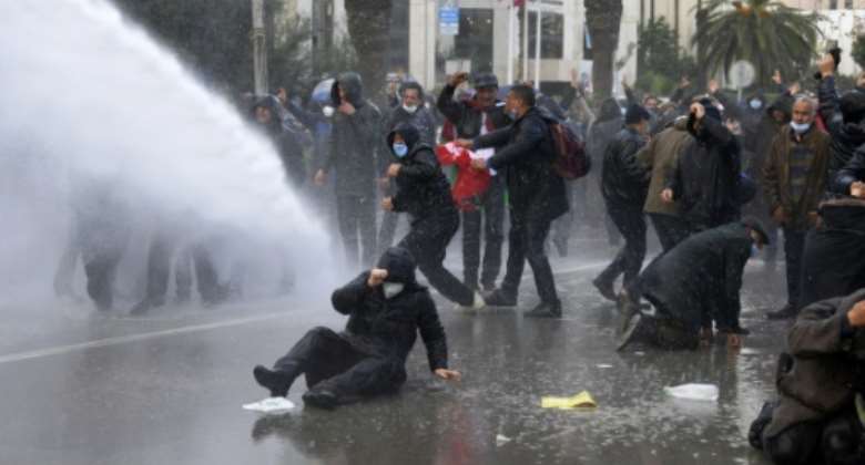 Tunisian demonstrations react after being hit by a water cannon during demonstrations against President Kais Saied, on the 11th anniversary of the Tunisian revolution in the capital Tunis.  By FETHI BELAID (AFP)