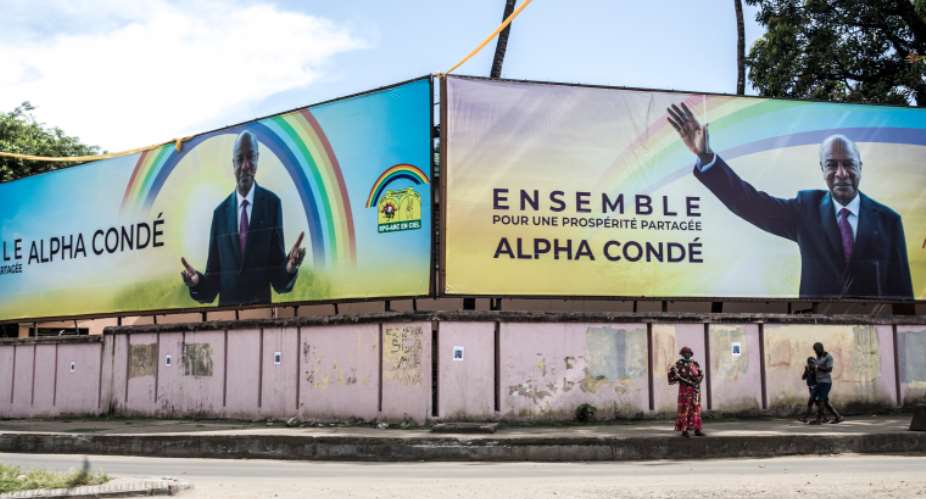 People walk under a campaign billboard for President Alpha Conde in Conakry, Guinea, on October 12, 2020. CPJ recently joined a letter calling on the Guinean government to maintain internet access throughout the presidential election. AFPJohn Wessels