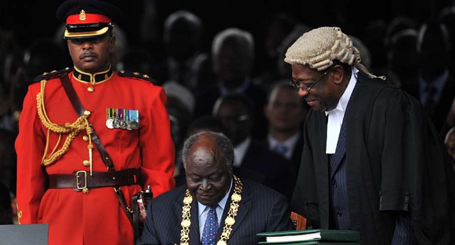 Former President Mwai Kibaki signs the new constitution in Nairobi in 2010 before former Attorney General Amos Wako. - Source: Tony KarumbaAFP via Getty Images