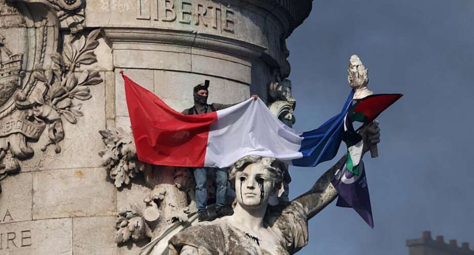 A masked protester stands on the statue of the Place de la Republique during a demonstration against the cost of living and rising fuel prices in Paris on Saturday, 17 October. - REUTERS - Jack Taylor