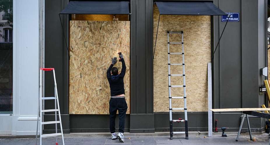 A worker installs plywood boards on a shop window in Lyon ahead of protests. -  Olivier Chassignole, AFP