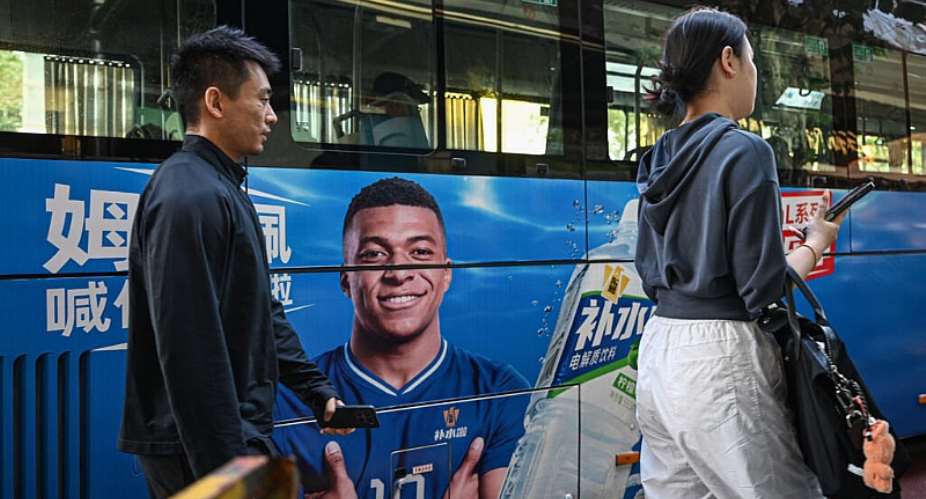 People walk past a bus featuring an advert starring French footballer Kylian Mbapp. -  Jade Gao, AFP