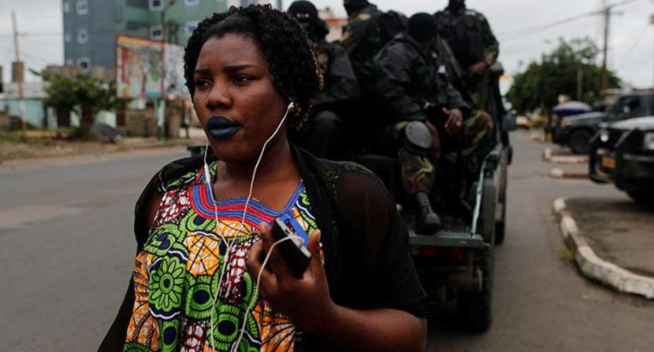 A woman walks past Rapid Intervention Battalion members as they patrol in the city of Buea in October 2018. CPJ and others are calling on the ACHPR to address human rights violations in Cameroon's Anglophone regions. ReutersZohra Bensemra