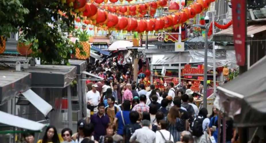 People walk along a crowded alleyway past stalls selling gifts and decorative items in the Chinatown district of Singapore on February 19, 2018. Singapore unveiled its 2018 budget on February 19, with economists predicting the city-state raising its goods