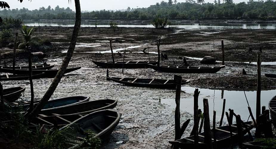 Oil smeared fishboats on oily mud in the river during low tide at K-Dere, near Bodo in the Niger Delta region  - Source: