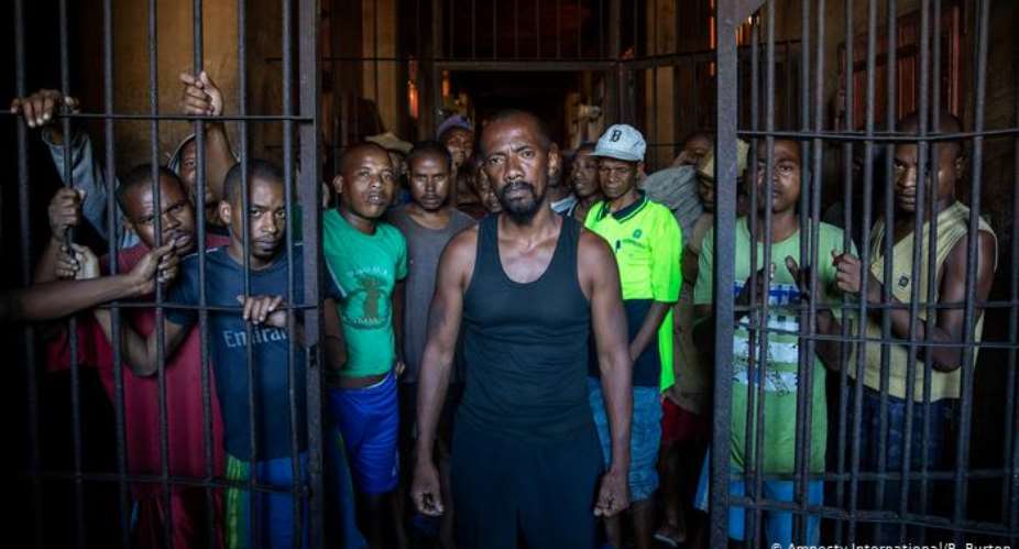 A group of pre-trial detainees in Madagascar stand behind half-opened prison bars