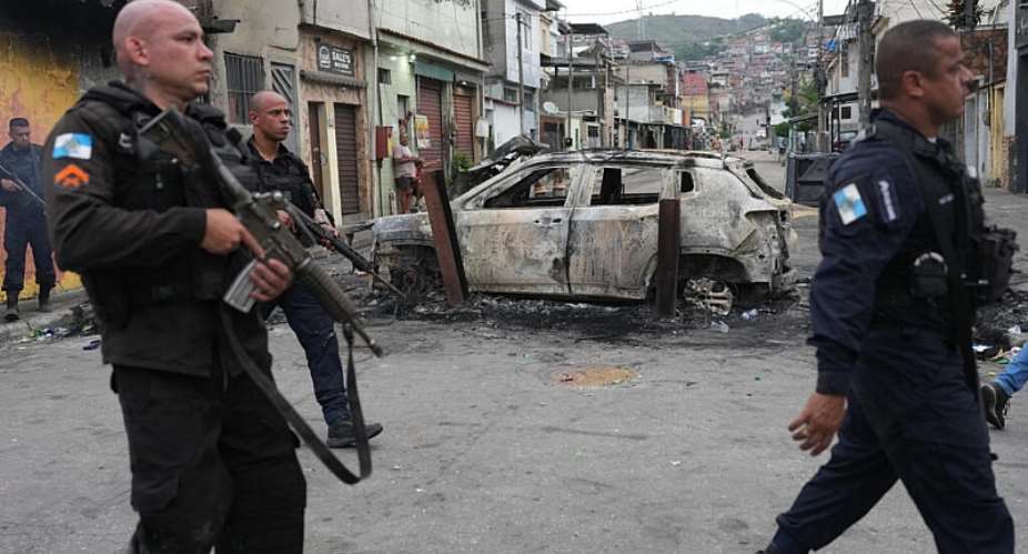 Police walk past a burned car used as a roadblock during a police operation against alleged drug traffickers in the Complexo do Alemao favela in Rio de Janeiro on Oct. 28, 2025. -  Silvia Izquierdo, AP