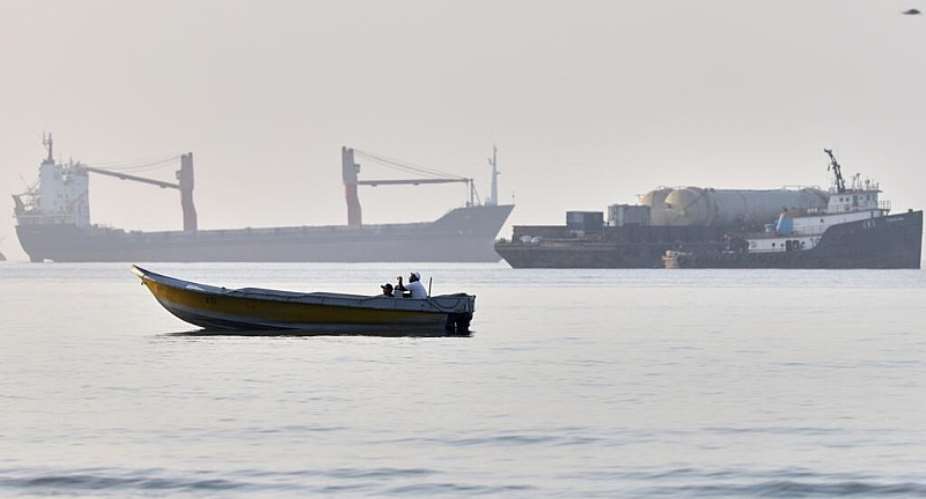 A small boat moves along the shoreline where an a cargo vessel, tugboat and industrial barge are all anchored in the Strait of Hormuz off Bandar Abbas, Iran,June 1, 2026 -  AP