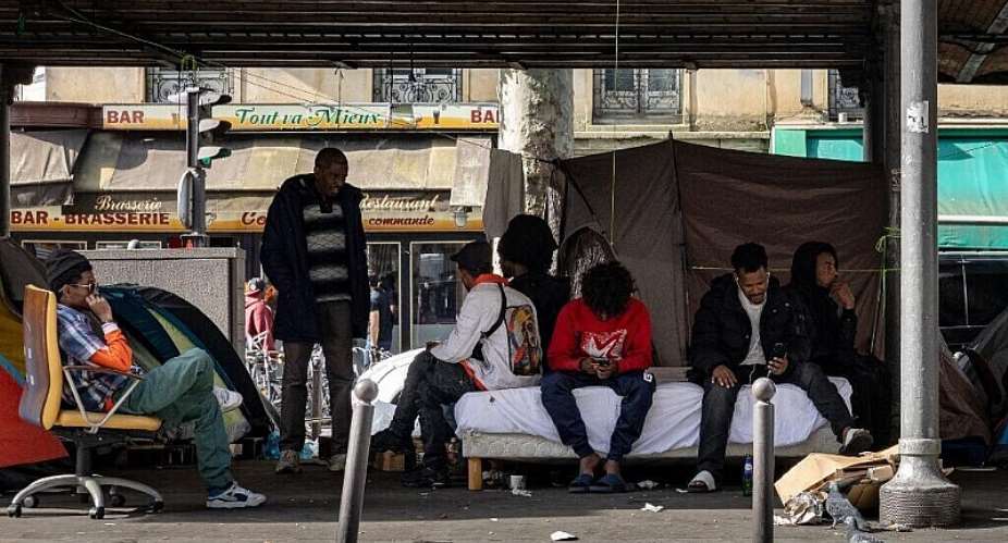 Migrants gather at a temporary migrant camp under an elevated section of the Metro in the La Chapelle district of Paris on June 6, 2026. - AFP - JOEL SAGET