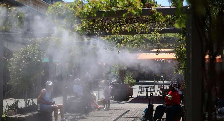 People sit in a shaded area under a water mist system to cool off in Bordeaux, south-western France, 17 June. - AFP - ROMAIN PERROCHEAU