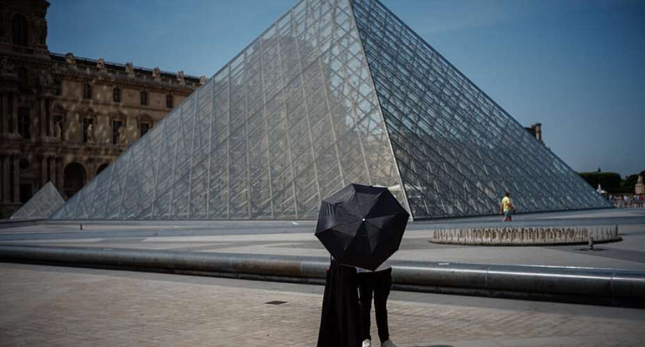 A couple protect themselves from the sun in front of the Louvre, which closed to the public on Wednesday as Paris recorded a record 40C. - AFP - DIMITAR DILKOFF