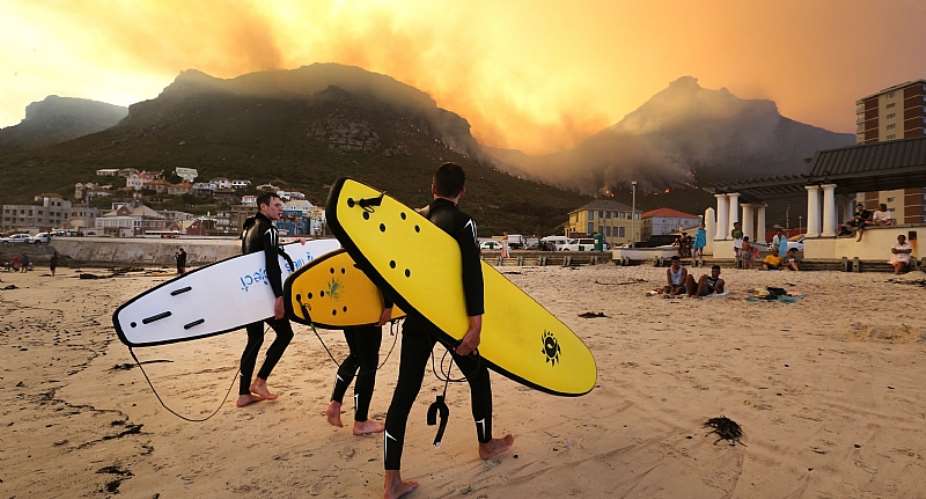 Surfers walk on the beach while the fire continues to blaze on the mountains behind them in 2015 in Cape Town, South Africa. - Source: Shelley ChristiansThe TimesGallo ImagesGetty Images