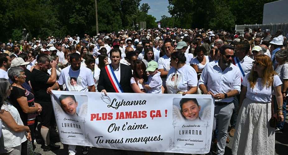Lyhannas father, Martial Bernard along with Fleurance mayor Gregory Bobbato and Lyhannas mother Charly Rameau hold a sign that says never again at the front of a march in tribute to Lyhanna in Fleurance, 7 June  2026. -  Lionel Bonaventure/AFP