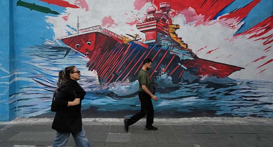 This photo taken on May 17, 2026 in downtown Tehran shows people walking past a mural depicting a US aircraft carrier under missile attack. -  AP Photo/Vahid Salemi (archive)