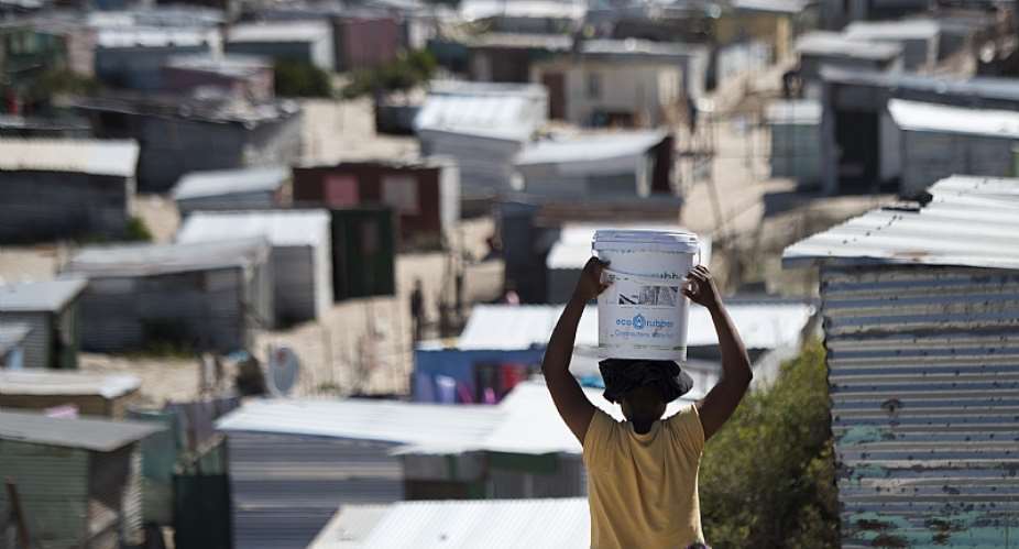 A woman carries a bucket of fresh water to an informal settlement in Khayelitsha,Cape Town. - Source: