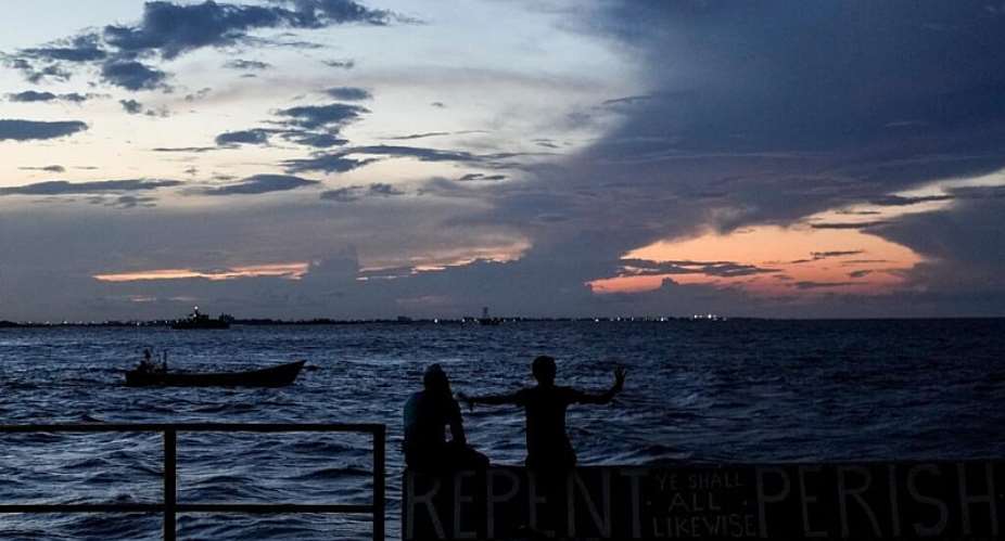 People sit on the seawall as the sun sets in Georgetown, Guyana,  Nov. 19, 2024. -  Matias Delacroix, AP