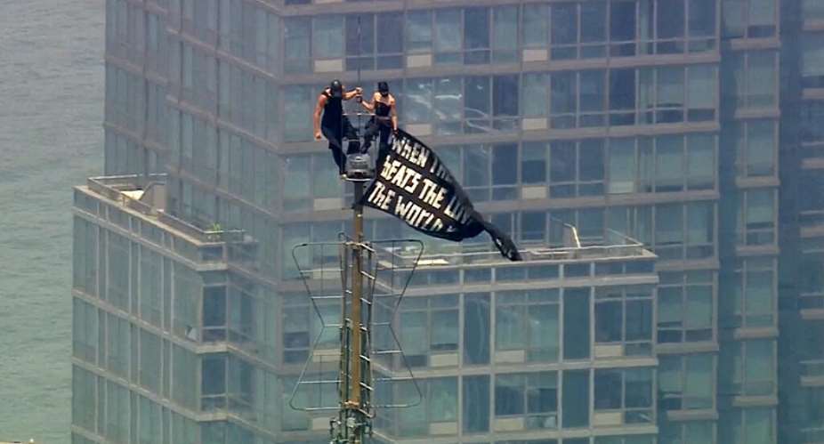 Two people stand on the tip of the antenna of the Empire State Building in New York while holding a banner, July 1, 2026 -  AP