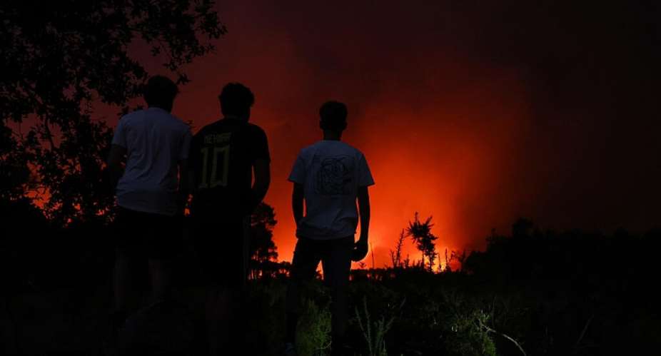 Youths watch from afar an area engulfed in flames during a wildfire in Le Porge, south-western France on July 22, 2026. - AFP - ROMAIN PERROCHEAU