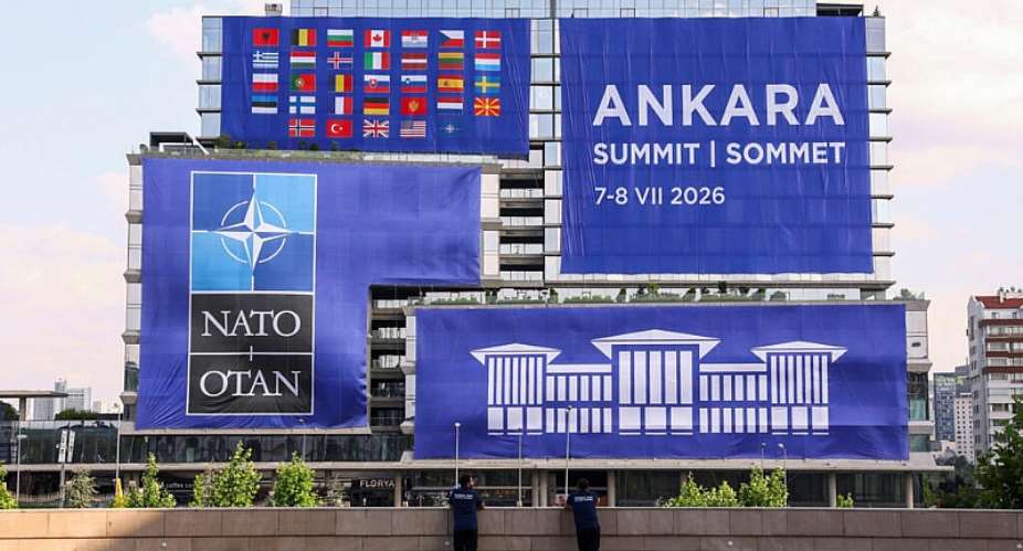 People stand near banners displaying logos and flags, on the sidelines of the NATO leaders Summit in Ankara, Turkey, July 7, 2026. -  Yves Herman / Reuters