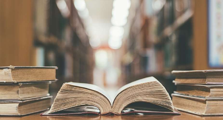 Book in library with old open textbook, stack piles of literature text archive on reading desk, and aisle of bookshelves in school study class room background for academic education learning concept - Shutterstock