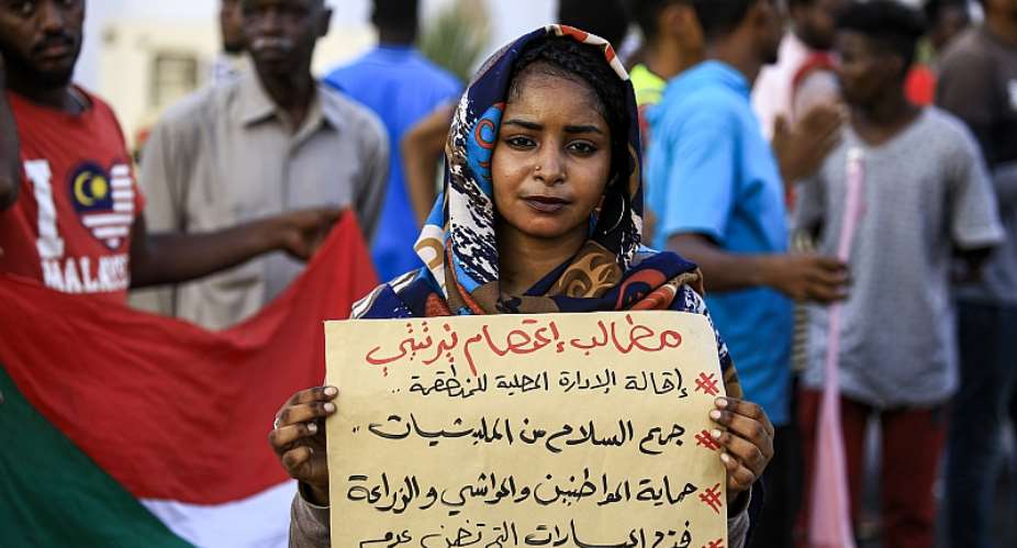 A demonstrator stands with a sign reading: amp;quot;Demands: sack the local authority, disarm militias, protect citizens, cattle, and farmland, and end friction between farmers and shepherdsamp;quot;, during a protest in Central Darfur.   - Source: Ashraf ShazlyAFP via Getty Images