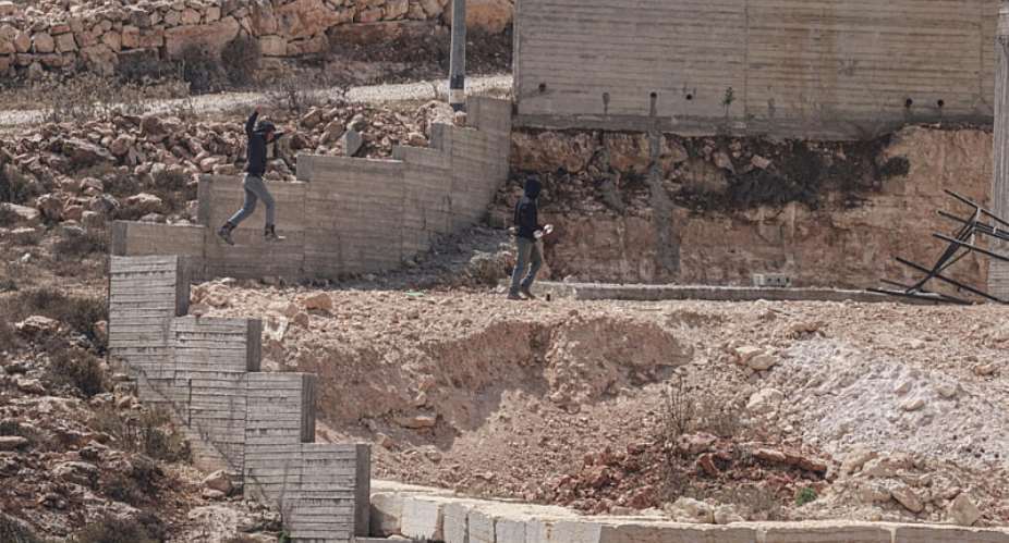 Israeli settlers jump over the garden wall as they make their way towards a Palestinian home under construction in the village of Qusra, which has faced escalating settler violence over the past month. -  Jaafar Ashtiyeh, AFP