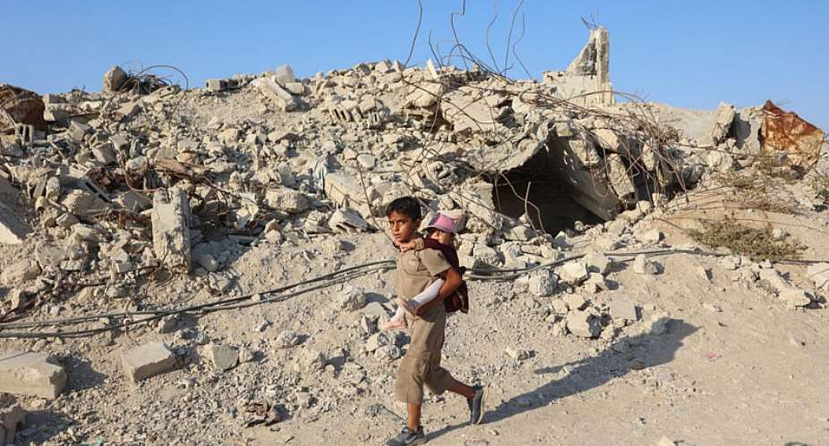 A Palestinian child carries a little girl on his back as he walks past the rubble of destroyed buildings in the Jabalia camp for Palestinian refugees in the northern Gaza Strip. -  Omar Al-Qattaa, AFP