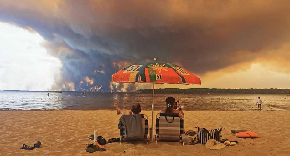 Beachgoers watch smoke rise from a wildfire at Moutchic beach in Lacanau, southwestern France, on 24 July 2026. A new UN report warns that heatwaves, wildfires and other climate extremes will become more frequent and severe as global warming exceeds 1.5C. - AFP - MAXIMILIEN LAMY
