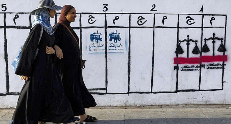 Women in Rabat walk past a wall displaying electoral symbols used by political parties participating in Moroccos legislative elections. - AFP - ABDEL MAJID BZIOUAT