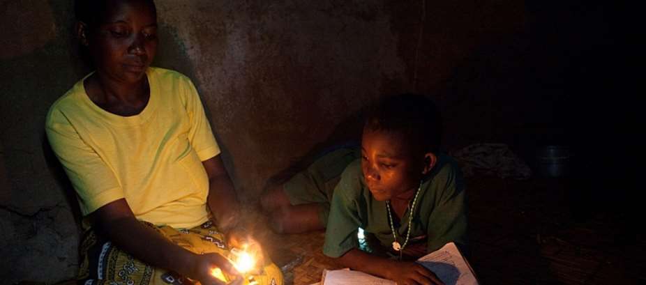 A mother using a kerosene lamp with her son indoors