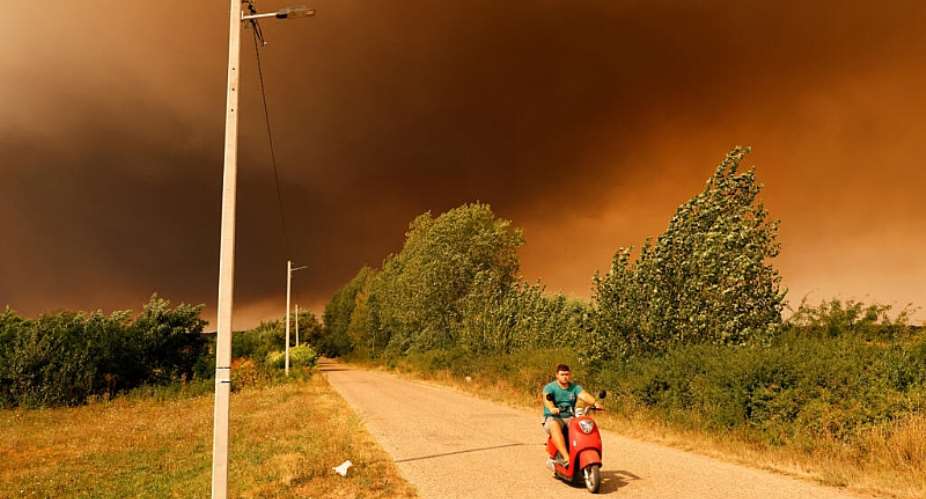 A man rides a scooter beneath a smoke-filled sky as a wildfire burns in Deliblatska Pescara, some 70 kilometres northeast of Belgrade, Serbia, on August 20, 2026. -  UROS ARSIC, AFP