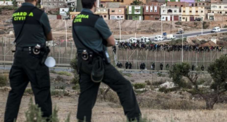 Spanish Guardia Civil watch as would-be immigrants from Africa sit atop a fence on Spain's tiny north African territory of Melilla on August 13, 2014.  By Jose Colon AFPFile