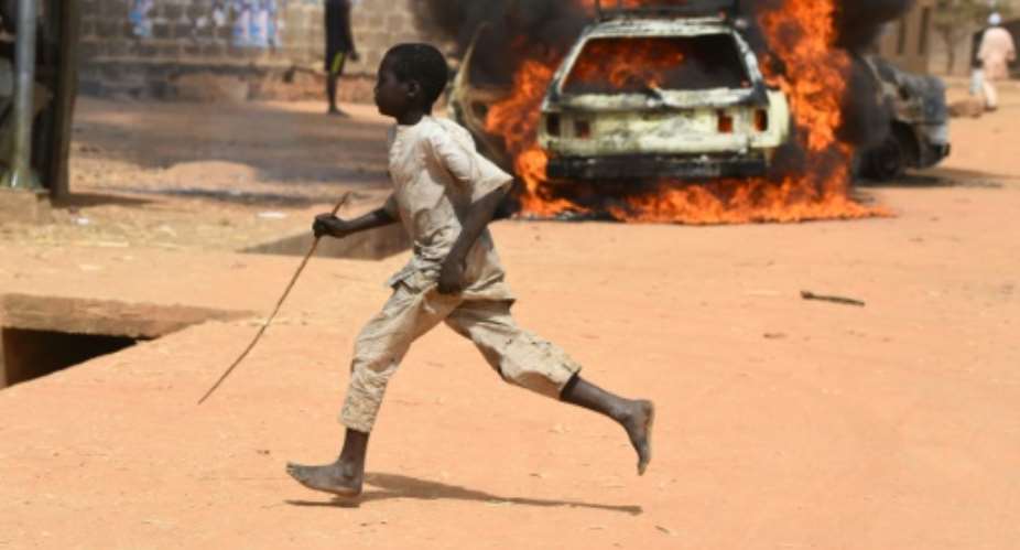 A boy runs off as cars are set on fire in Kofa.  By PIUS UTOMI EKPEI AFP
