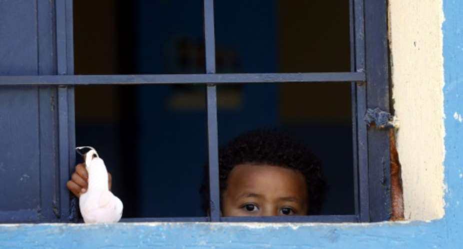 A child from a family of African migrants peeks out from a window at Libyan detention center, among thousands who have tried in recent years to flee to Europe via the North African country.  By Mahmud TURKIA AFP