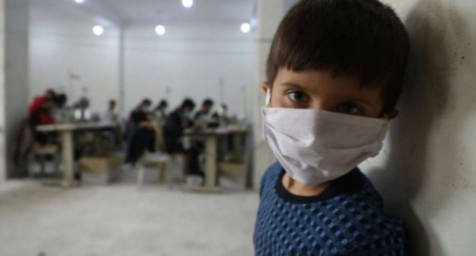 A child looks on as volunteers gather in a sewing workshop to make protective face-masks in the northeastern Syrian city of Idlib.  By AAREF WATAD AFPFile